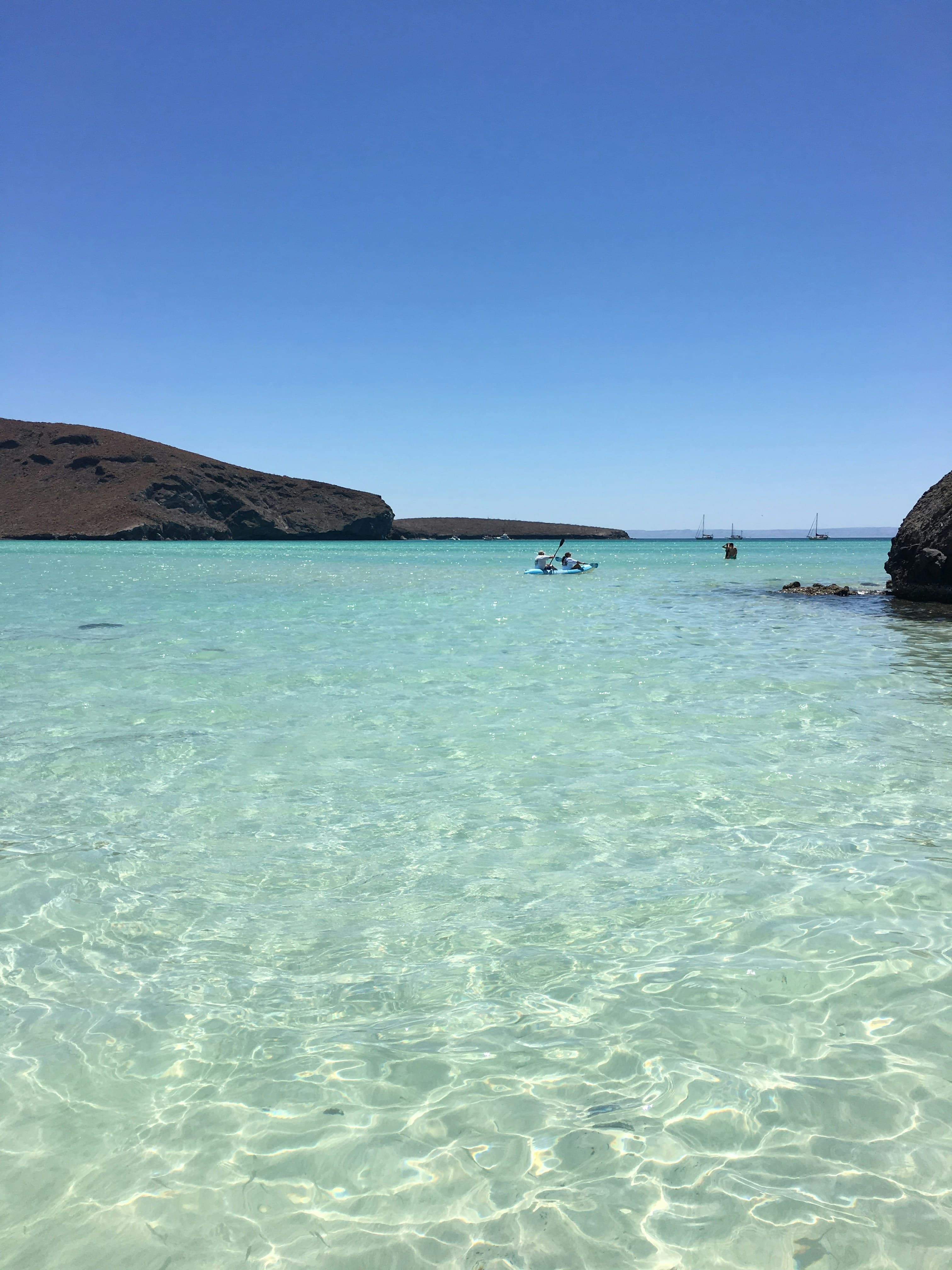 Two kayakers paddling through crystal-clear turquoise Caribbean waters near a tropical island